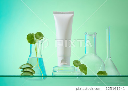 Unlabeled tubes stand on round glass pedestals decorated with green gotu kola leaves. Aloe vera pieces are stacked on top of each other. Laboratory flasks contain liquid and gotu kola plants. 125161241