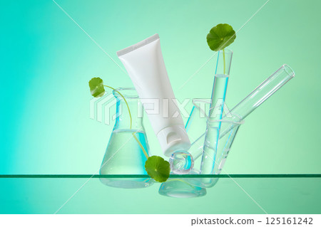 Composition of laboratory instruments such as flasks, beaker, test tubes, and Centella asiatica are placed scattered for decoration. White tube mockup show at an angle, used for cosmetic advertising. 125161242