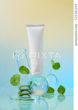 Portrait photo of white cream tube placed on a glass globe, surrounded by gotu kola plants with fresh leaves. Cut aloe vera placed in petri dishes. Essential cosmetic ingredients for skincare. Portrait photo of white cream tube placed on a glass globe, surrounded by gotu kola plants with fresh leaves. Cut aloe vera placed in petri dishes. Essential cosmetic ingredients for skincare. 125161247