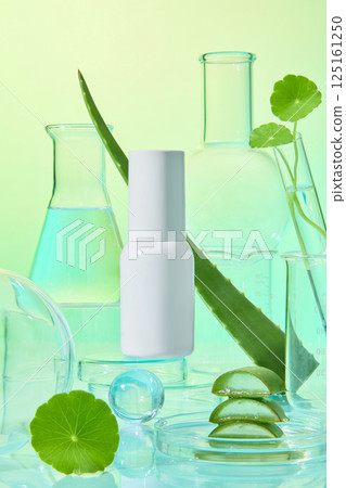 Cylindrical cosmetic bottles and measuring cups containing liquids placed around pennywort plants. Aloe vera pieces are stacked on top of each other in petri dishes. Modern laboratory concept. 125161250