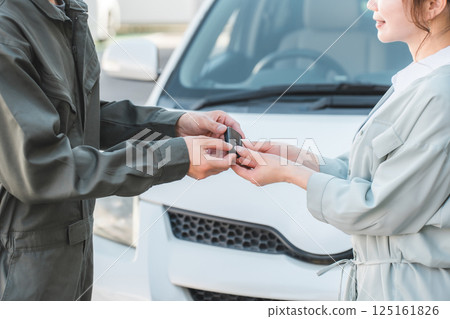 Male auto mechanic staff handing over car keys to female customer Male auto mechanic staff handing over car keys to female customer 125161826
