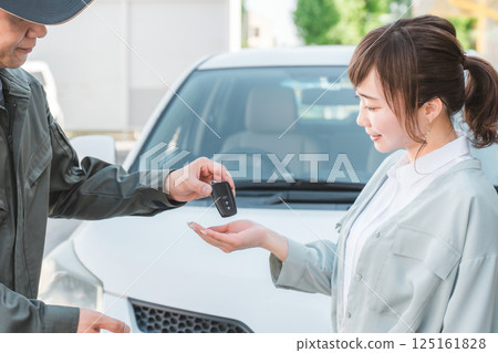 Male auto mechanic staff handing over car keys to female customer 125161828