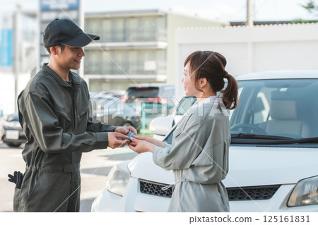 A male auto mechanic staff member taking car keys from a female customer 125161831