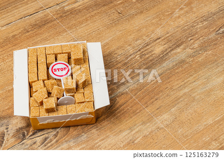 Brown sugar cubes in a box with a stop sign on a wooden surface 125163279