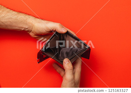 Financial struggle is evident as a man inspects his empty wallet Financial struggle is evident as a man inspects his empty wallet 125163327