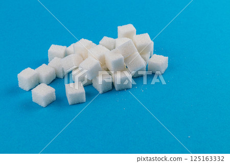 Sugar cubes scattered on a solid blue background creating a visual contrast Sugar cubes scattered on a solid blue background creating a visual contrast 125163332