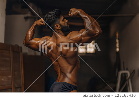 Bodybuilder Showcasing Impressive Muscle Definition in an Indoor Gym Setting During Afternoon Training 125163436