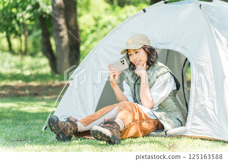Woman enjoying camping/glamping using smartphone at campsite 125163588