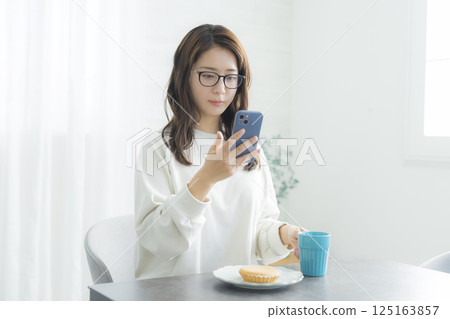 A woman looking at her smartphone while eating breakfast 125163857