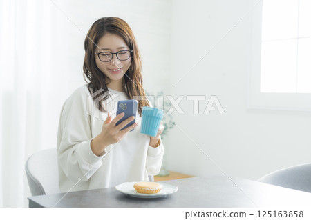 A woman looking at her smartphone while eating breakfast A woman looking at her smartphone while eating breakfast 125163858