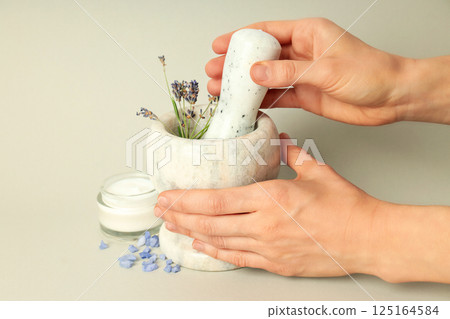 Cosmetic jar with cream, lavender in mortar and female hands on gray background 125164584