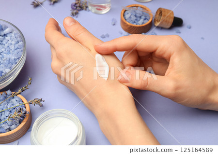 Lavender, sea salt and female hands with cream on purple background, close up 125164589