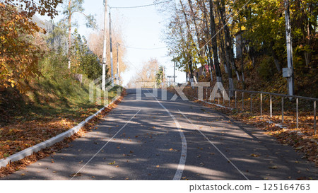 A serene and tranquil uphill road that is surrounded by stunning colorful autumn foliage and clear blue skies 125164763