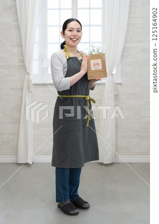 A woman wearing an apron holding a bag of rice flour 125164902