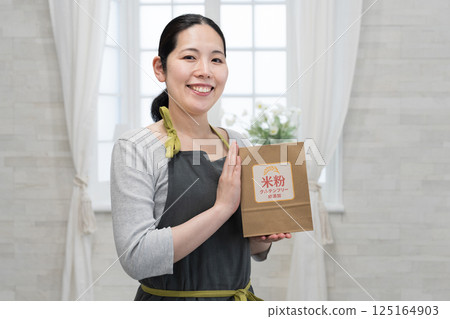 A woman wearing an apron holding a bag of rice flour 125164903
