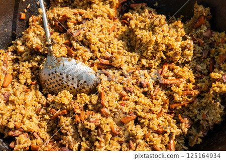 Large cauldron with pilaf. Street food sales. Hot rice pilaf with meat and spices. Large cauldron with pilaf. Street food sales. Hot rice pilaf with meat and spices. 125164934