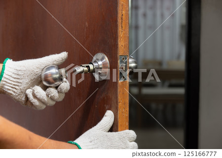 Locksmith on wood door with screwdriver for repair or fix silver knob. 125166777