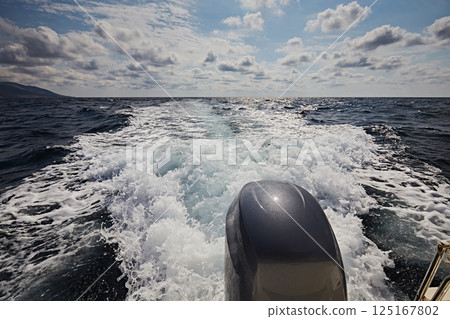A boat motor trail in the sea and a blue sky with clouds 125167802