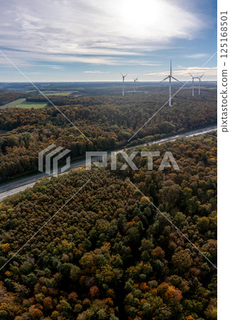 Drone aerial view with highway passing through autumn forest, at horizon wind turbines 125168501