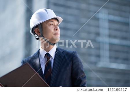 一名西裝革履的男子站在建築工地，手裡拿著一份文件 125169217