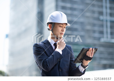 建築工地上,一名男子一手拿著平板電腦,一邊思考 建築工地上,一名男子一手拿著平板電腦,一邊思考 125169337