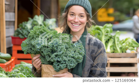 Smiling woman holding a bunch of fresh kale at a farmer market, dressed warmly and surrounded by organic vegetables. Smiling woman holding a bunch of fresh kale at a farmer market, dressed warmly and surrounded by organic vegetables. 125169364