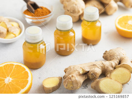 Turmeric energy shot immune drink with ginger root and ripe oranges on light background.Macro. 125169857