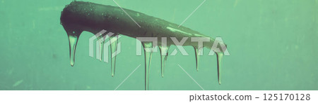 An icicle dangles with a sharp point and dripping tip against a grunge background. 125170128