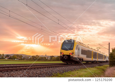 Passenger train traveling at sunrise near a german village Passenger train traveling at sunrise near a german village 125170200