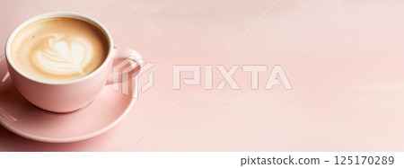 A top-view shot of a cappuccino in a pastel-colored cup, featuring a delicate heart-shaped latte art design. The coffee sits against a soft, textured background 125170289