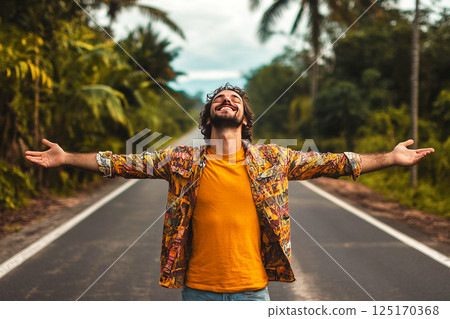 A joyful summer scene featuring a man with his hands raised, basking in the warmth of the sun. The image captures a carefree and happy moment, possibly with palms in the background 125170368
