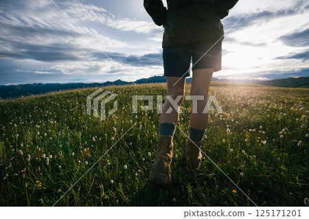 Hiker legs wearing leather hiking boots walking on beautiful flowering grassland 125171201