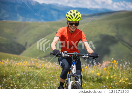 Woman riding mountain bike on beautiful flowering grassland mountain top Woman riding mountain bike on beautiful flowering grassland mountain top 125171203
