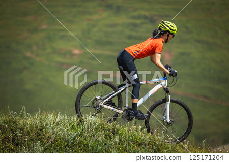 Woman riding mountain bike on beautiful flowering grassland mountain top 125171204