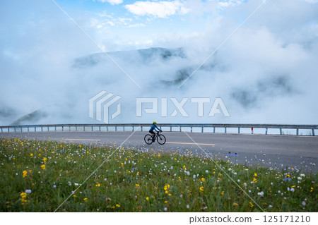 Woman riding bike on flowering grassland mountain top trail Woman riding bike on flowering grassland mountain top trail 125171210