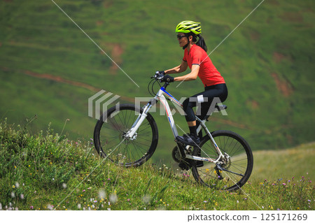 Fitness aisan woman riding mountain bike on beautiful flowering grassland mountain top 125171269
