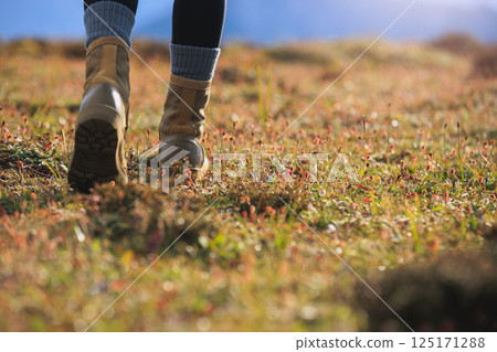 Hiker legs wearing leather boots hiking on high altitude mountain top Hiker legs wearing leather boots hiking on high altitude mountain top 125171288
