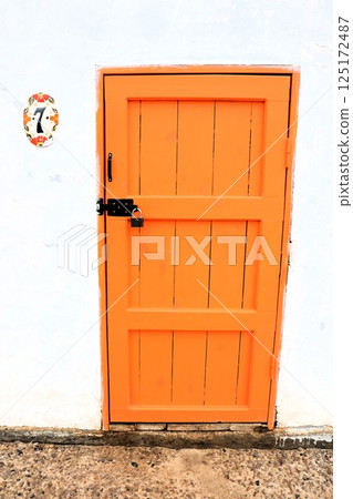 A Vibrant Orange Door Set Against a White Wall, Showcasing Beauty and Artistic Charm A Vibrant Orange Door Set Against a White Wall, Showcasing Beauty and Artistic Charm 125172487