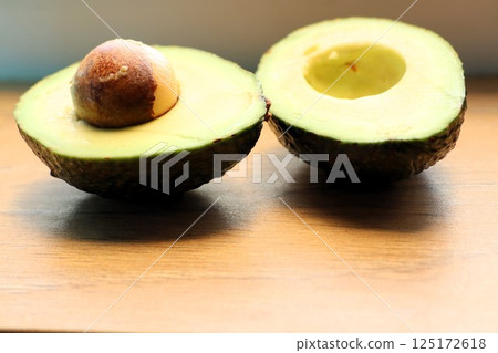 Fresh Avocado Halves with Pit Placed Beautifully on a Wooden Surface for Presentation Fresh Avocado Halves with Pit Placed Beautifully on a Wooden Surface for Presentation 125172618