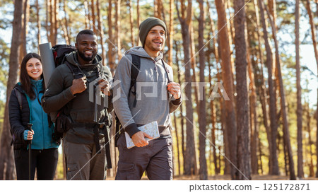 Three cheerful multiracial friends hiking by forest, going towards free space, side view 125172871