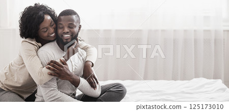 Loving wife cuddling husband from the back while sitting on bed together, enjoying weekend. Copy space Loving wife cuddling husband from the back while sitting on bed together, enjoying weekend. Copy space 125173010