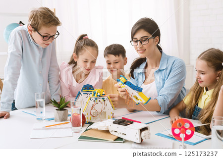 A group of young students are engaged in a STEM class, working together to build a robot. A teacher guides them, while they follow instructions and use their creativity to solve problems. 125173237