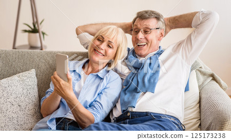 Happy mature couple using cellphone, surfing internet online, sitting on sofa at home, free space 125173238