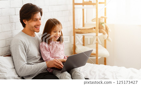 Little girl spending time with her daddy, using laptop in bedroom, copy space 125173427
