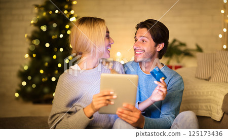 Couple buying Christmas gifts online, using tablet and credit card, sitting in front of Christmas tree Couple buying Christmas gifts online, using tablet and credit card, sitting in front of Christmas tree 125173436