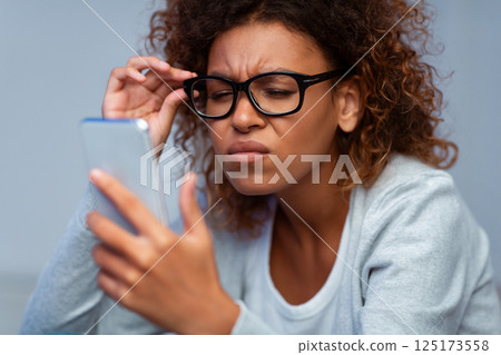 Girl with bad sight trying to read message on cellphone, wearing glasses Girl with bad sight trying to read message on cellphone, wearing glasses 125173558