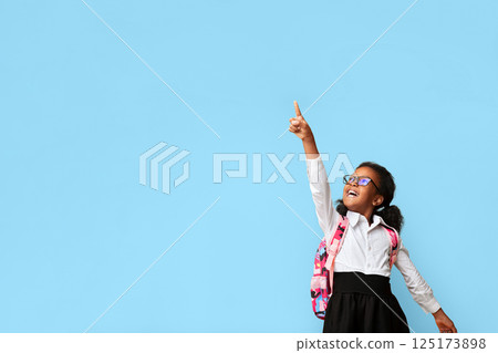 Look There Concept. Cute Afro Schoolgirl Pointing Finger Up Showing Something Over Yellow Studio Background. Copy Space 125173898