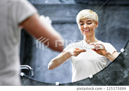 Skincare Concept. Joyful Middle-Aged Woman Applying Micellar Water On Cotton Pad, Cleansing And Caring For Mature Skin Standing In Bathroom. 125173899