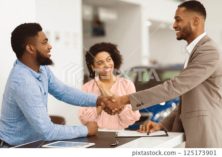 Afro Spouses Buying Car Handshaking With Seller Man Standing In Dealership Office. Selective Focus 125173901