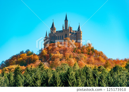 Hohenzollern castle on the hilltop, surrounded by autumn forest, under a blue sky 125173918